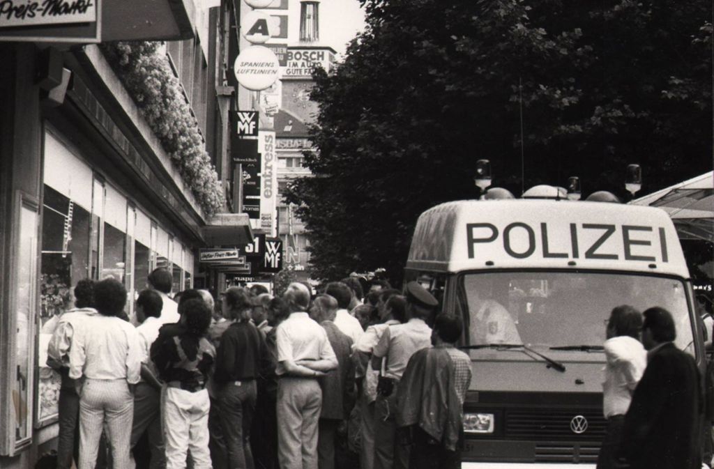Fußballfans bei der EM 1988 vor einem Schaufenster in der Fußgängerzone der Königstraße – Polizeibeamte fahren heran und schauen auch mit zu.