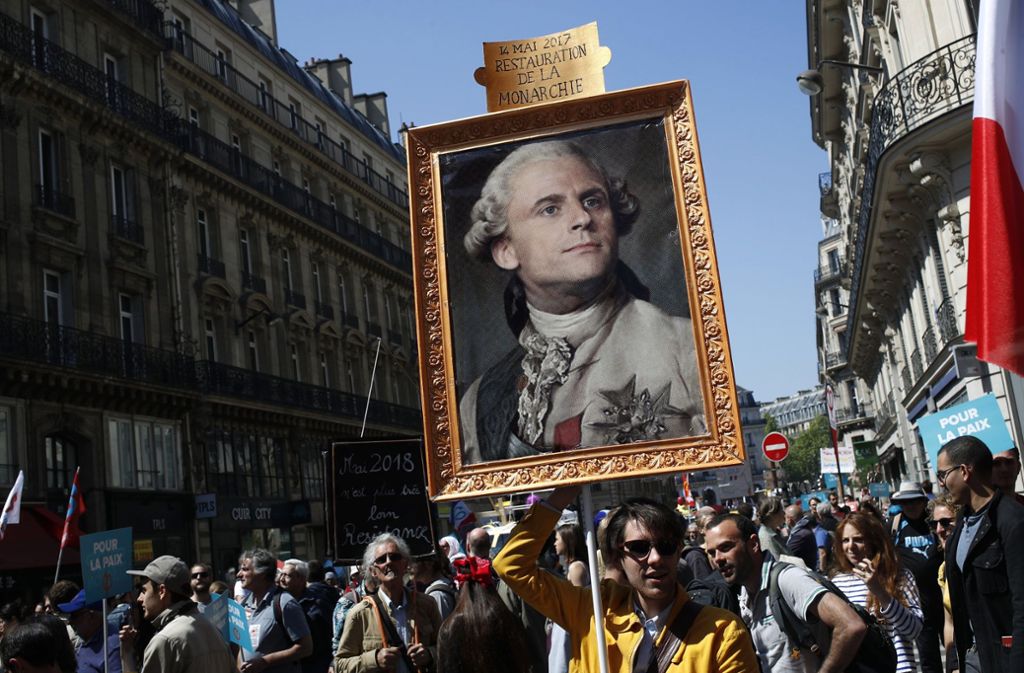 Demonstranten tragen ein Foto von Emmanual Macron als König Louis XVI durch die Straßen von Paris. Sie sehen Parallelen zu dem ungeliebten Monarchen vor über 200 Jahren. Damals löste die Demokratie die Monarchie ab.
