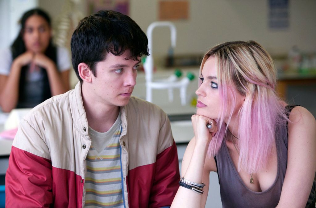 In der brillanten Netflix-Serie „Sex Education“ läuft die Hauptdarstellerin Emma Mackey mit einem schlampig-punkigen Look herum (auf dem Foto mit Hauptdarsteller Asa Butterfield). Dazu passend trägt sie Haare schön unordentlich in einem heraus gewachsenen  „Two-Tone Blond-Pink“.