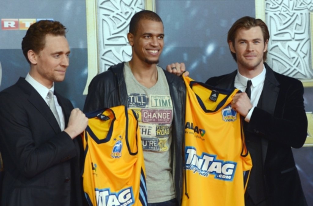 Alba-Spieler Alex King (Mitte) überreicht dem britischen Schauspieler Tom Hiddleston (links) und dem australischen Schauspieler Chris Hemsworth vor der Deutschlandpremiere des Films Thor - The Dark Kingdom Trikots der Basketball-Mannschaft.